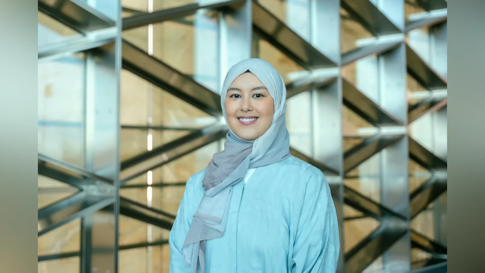 Portrait picture, smiling, blue Abaya, blue-brown gradient Hijab, and brown background with metal beems